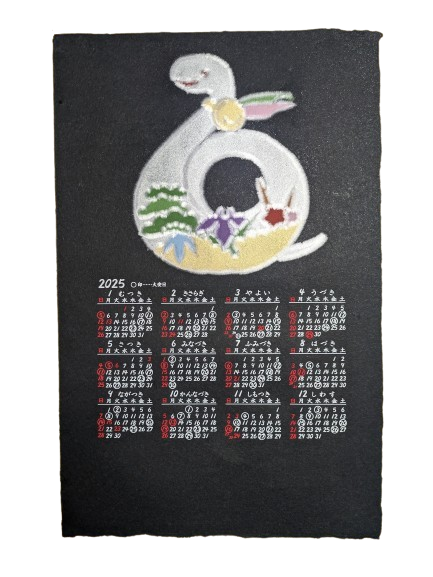 2025年、巳年用の手漉き和紙カレンダーの全体を写した写真です。こちらは「花へび柄」。ベースは黒い和紙で、上部にはへびの絵柄が、下部には12カ月分の日付が記載されています。絵柄は白いへびが向かって左側を向いているもの、体の下半分には松や菖蒲のような花も描かれています。こちらは「ひっかき技法」を用いて表現されており、印刷ではない華やかな風合いが特徴です。松久永助紙店オンラインショップでは他にも次のような和紙商品を取り扱っています。和紙(楮紙/こうぞ紙・マニラ麻・落水紙・本美濃紙/那須楮・墨流し)、和紙雑貨(カードケース・さついれ・干支カレンダー)、和紙文具(ノート・マスキングテープ・和紙はがき)、紙布雑貨(手ぬぐい・ワインバッグ・トートバッグ・ポーチ・ランチョンマット・マルチクロス)、生活雑貨(アクセサリー・ハンカチ・ハンドタオル・フェイスタオル・バスタオル・サウナタオル/ロングタオル・靴下/ソックス・アームカバー・信玄袋)、和紙布(帆布・ガーゼ・シャツ地・ニット・天竺・ヘリンボーン・手ぬぐい・コットン混・リネン混)、和紙糸(Kamito糸柱・ネロ・編み物用・織物用・刺繍用・玉売り・綛売り・コーン売り)。