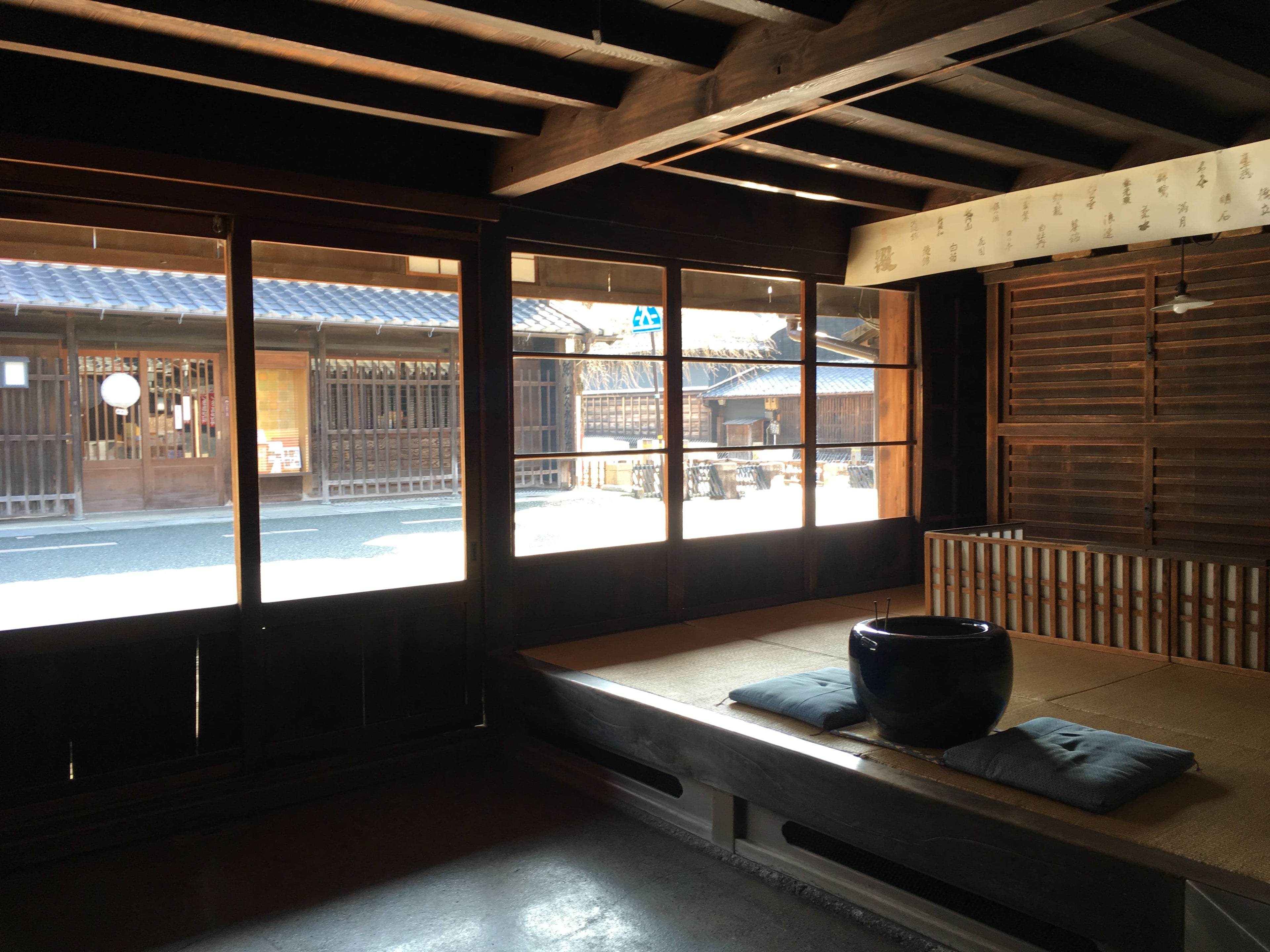 松久永助紙店の現店舗向かいにある帳場の中の様子がうつっています。画面右の手前側には、火鉢と座布団が2枚うつっており、その奥側には番頭台が見えます。また正面はガラス戸で、松久永助紙店の現店舗と、うだつの上がる町並みの目の字通りが見えます。■松久永助紙店では紙糸(和紙糸)、紙布(和紙布)、美濃和紙靴下(和紙ソックス)、美濃和紙タオルなどの美濃和紙をつかった生活雑貨などを取り扱っています。主な商品は、和紙・美濃和紙(楮紙/こうぞ紙・マニラ麻・落水紙・本美濃紙/那須楮・墨流し)、和紙雑貨(カードケース・さついれ・干支カレンダー)、和紙文具(ノート・マスキングテープ・和紙はがき)、紙布雑貨(手ぬぐい・ワインバッグ・トートバッグ・ポーチ・ランチョンマット・マルチクロス)、生活雑貨(アクセサリー・ハンカチ・ハンドタオル・フェイスタオル・バスタオル・サウナタオル/ロングタオル・靴下/ソックス・アームカバー・信玄袋)、和紙布(帆布・ガーゼ・シャツ地・ニット・天竺・ヘリンボーン・手ぬぐい・コットン混・リネン混)、和紙糸(Kamito糸柱・ネロ・編み物用・織物用・刺繍用・玉売り・綛売り・コーン売り)です。