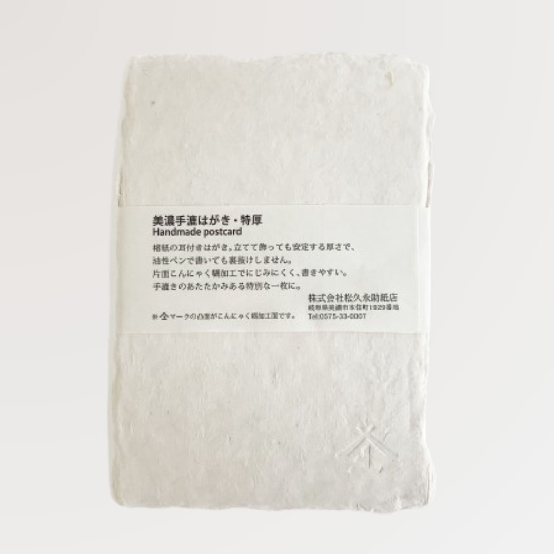 白い背景、「特厚美濃和紙手漉はがき」の裏面を撮影した写真です。商品真ん中には、商品説明と店名・住所・電話番号を記載した商品帯が横方向にまかれています。右下にはエンボス加工されたロゴマーク(裏)が見えます。松久永助紙店オンラインショップでは他にも次のような和紙商品を取り扱っています。和紙(楮紙/こうぞ紙・マニラ麻・落水紙・本美濃紙/那須楮・墨流し)、和紙雑貨(カードケース・さついれ・干支カレンダー)、和紙文具(ノート・マスキングテープ・和紙はがき)、紙布雑貨(手ぬぐい・ワインバッグ・トートバッグ・ポーチ・ランチョンマット・マルチクロス)、生活雑貨(アクセサリー・ハンカチ・ハンドタオル・フェイスタオル・バスタオル・サウナタオル/ロングタオル・靴下/ソックス・アームカバー・信玄袋)、和紙布(帆布・ガーゼ・シャツ地・ニット・天竺・ヘリンボーン・手ぬぐい・コットン混・リネン混)、和紙糸(Kamito糸柱・ネロ・編み物用・織物用・刺繍用・玉売り・綛売り・コーン売り)。