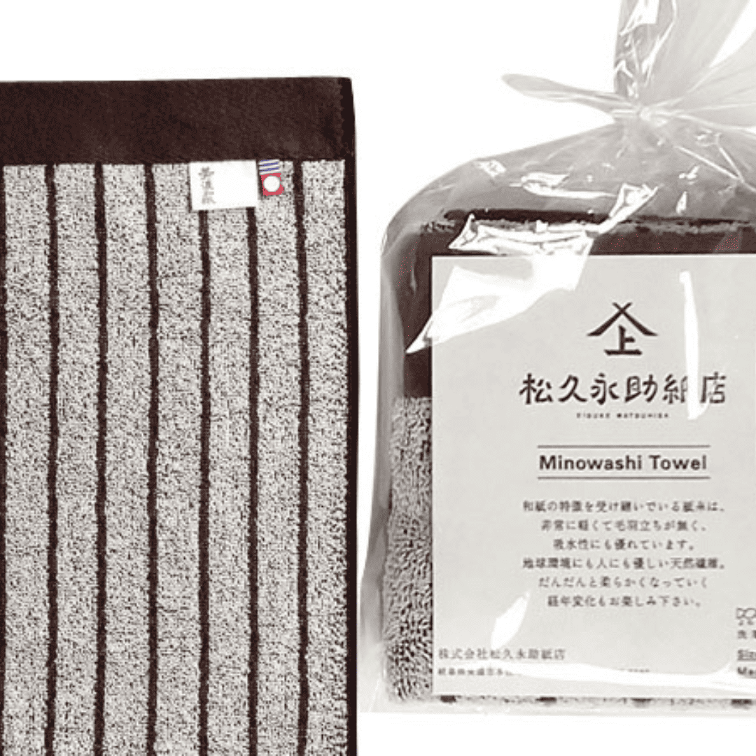 美濃和紙タオル、ストライプ柄の茶色、包装された状態(右)と広げられた状態のアップ(左)がうつっています。包装されている方は、正方形に小さく畳まれ、店名、商品名、商品説明が記載された紙(畳んだタオルと同じくらいの大きさ)とともに、透明の袋でに入れられています。袋の口は紙糸をリボン結びにして縛られています。広げられた方には2種類のタグが付いている様子も見えます。タグは「美濃和紙」とかかれたもの(右側)と、今治タオルのブランドロゴ(左側)です。下記は関連するキーワードになります。ベーシック 使いやすい オフィス 学校 プレゼント オールシーズン 機能的 ギフト こだわり 日本製 ちょっといいタオル 松久永助紙店 オンラインショップ