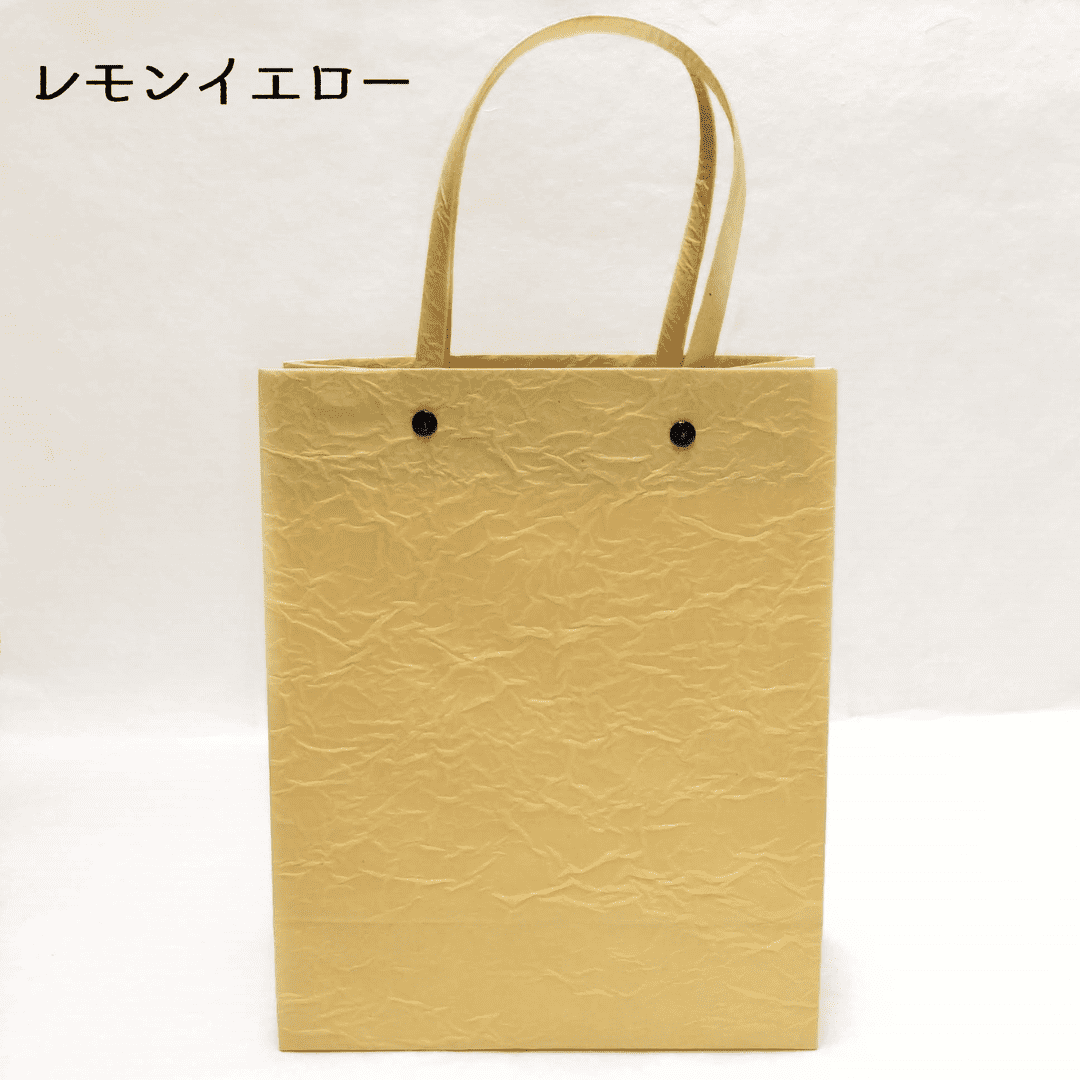 美濃和紙のマスキングテープ原紙を使った、手提げバッグの黄色がうつっています。持ち手と本体を固定する(繋ぐ)金具は黒です。下記は関連するキーワードになります。美濃和紙 マスキングテープ アップサイクル 環境に優しい 紙袋 カバン 和紙雑貨 カジュアル 和装 和小物 差し色 黄色 推しカラー パステルカラー 松久永助紙店 オンラインショップ