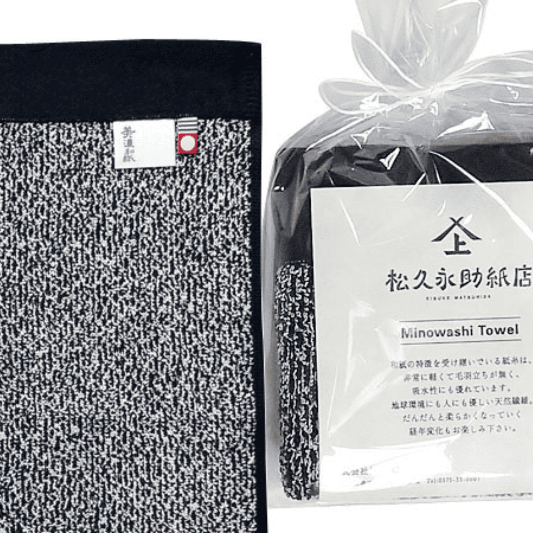美濃和紙タオル、ソリッドの黒、包装された状態(右)と広げられた状態のアップ(左)がうつっています。包装されている方は、正方形に小さく畳まれ、店名、商品名、商品説明が記載された紙(畳んだタオルと同じくらいの大きさ)とともに、透明の袋でに入れられています。袋の口は紙糸をリボン結びにして縛られています。広げられた方には2種類のタグが付いている様子も見えます。タグは「美濃和紙」とかかれたもの(右側)と、今治タオルのブランドロゴ(左側)です。下記は関連するキーワードになります。無地 父の日 母の日 ギフト お祝い 学校 入学 卒業 ビジネス ご挨拶 配りもの お返し おすすめ 美濃和紙タオル 紙糸 松久永助紙店 オンラインショップ