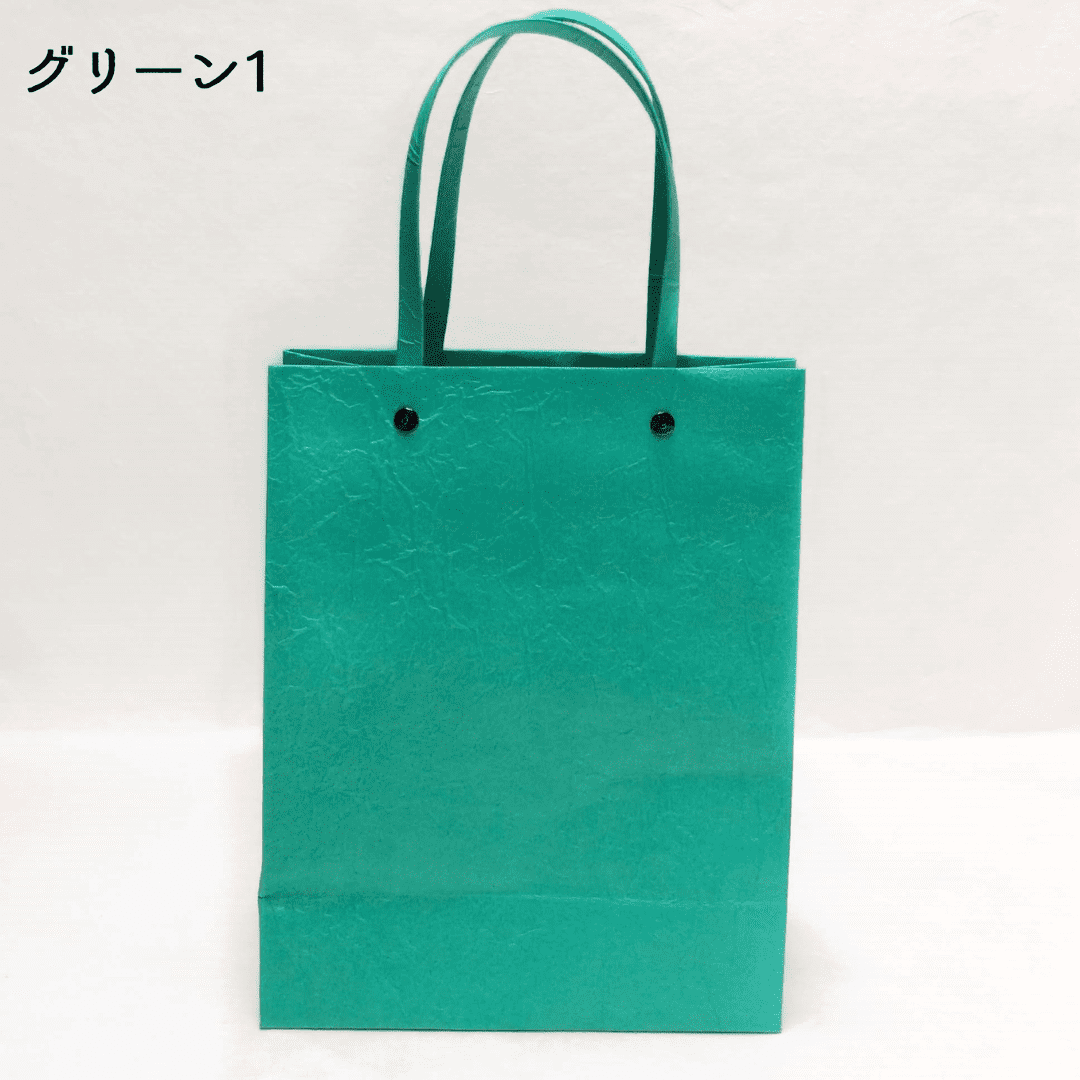 美濃和紙のマスキングテープ原紙を使った、手提げバッグの緑色がうつっています。持ち手と本体を固定する(繋ぐ)金具は黒です。下記は関連するキーワードになります。和紙カバン 紙袋 手提げ 美濃和紙 和装 和小物 和紙雑貨 手作り 日本製 ちょっと変わった 緑 推しカラー パステルカラー アクセント 松久永助紙店 オンラインショップ
