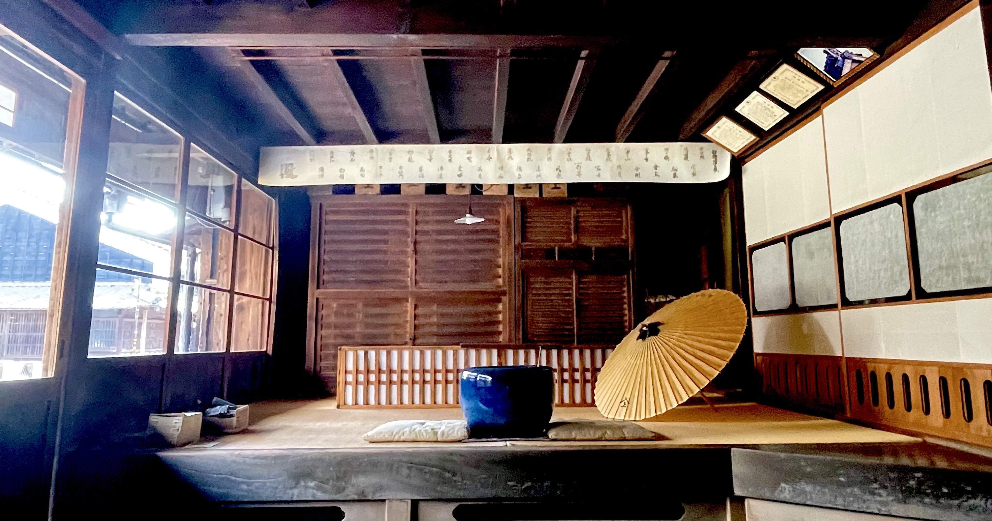 松久永助紙店の現店舗向かいにある、帳場の室内の様子がうつっています。日本家屋で、道路に面した扉はガラスがはめこまれ、光がたくさん入ってきています。土間から一段あがると番頭台や火鉢、和傘が鑑賞できるようになっています。■松久永助紙店では紙糸(和紙糸)、紙布(和紙布)、美濃和紙靴下(和紙ソックス)、美濃和紙タオルなどの美濃和紙をつかった生活雑貨などを取り扱っています。主な商品は、和紙・美濃和紙(楮紙/こうぞ紙・マニラ麻・落水紙・本美濃紙/那須楮・墨流し)、和紙雑貨(カードケース・さついれ・干支カレンダー)、和紙文具(ノート・マスキングテープ・和紙はがき)、紙布雑貨(手ぬぐい・ワインバッグ・トートバッグ・ポーチ・ランチョンマット・マルチクロス)、生活雑貨(アクセサリー・ハンカチ・ハンドタオル・フェイスタオル・バスタオル・サウナタオル/ロングタオル・靴下/ソックス・アームカバー・信玄袋)、和紙布(帆布・ガーゼ・シャツ地・ニット・天竺・ヘリンボーン・手ぬぐい・コットン混・リネン混)、和紙糸(Kamito糸柱・ネロ・編み物用・織物用・刺繍用・玉売り・綛売り・コーン売り)です。