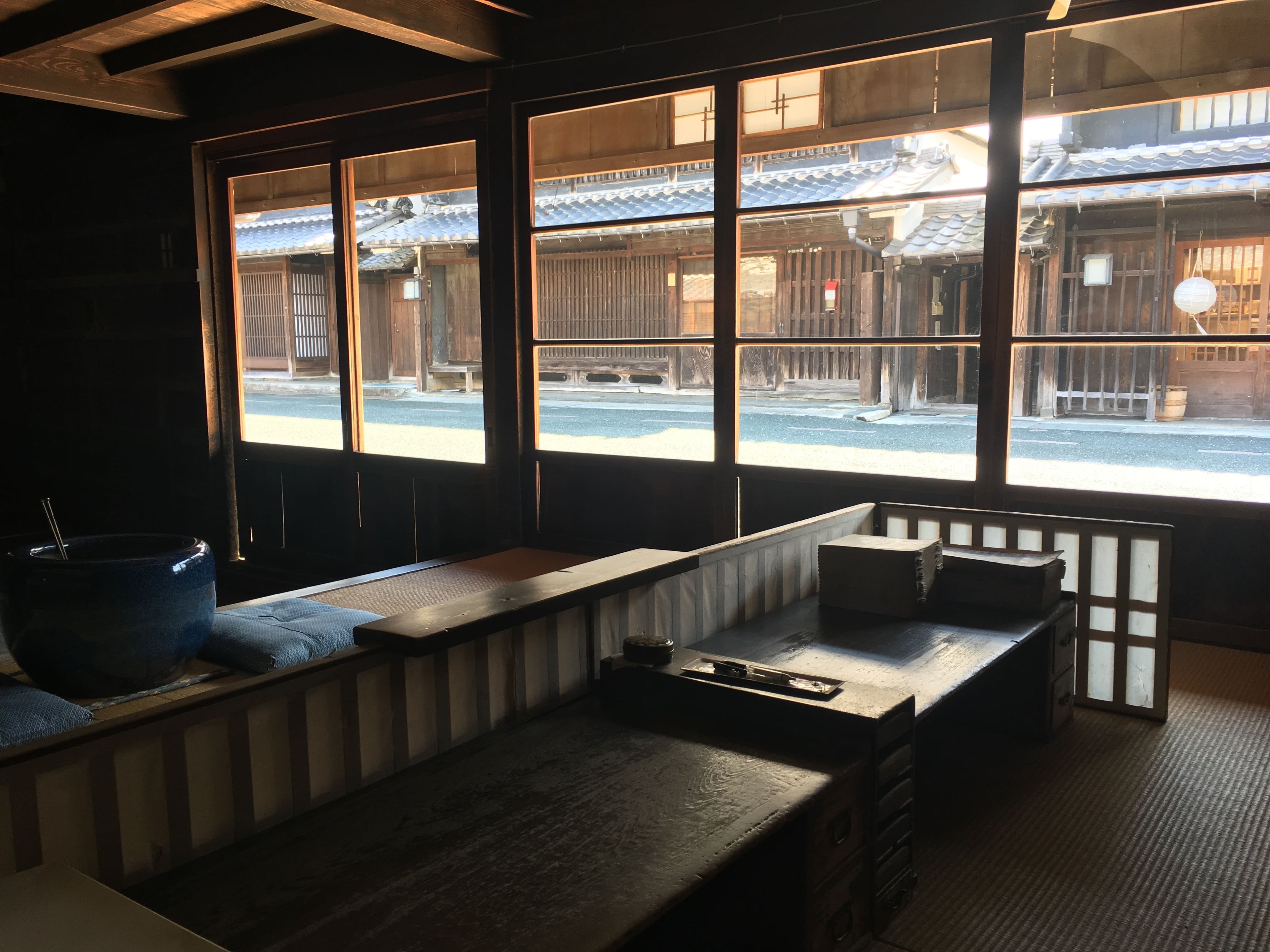 松久永助紙店の現店舗向かいにある帳場の中の様子がうつっています。手前側には番頭台の机がうつっており、机の向こうには青い火鉢と座布団が2枚うつっています。また正面はガラス戸で、松久永助紙店の現店舗と、うだつの上がる町並みの目の字通りが見えます。■松久永助紙店では紙糸(和紙糸)、紙布(和紙布)、美濃和紙靴下(和紙ソックス)、美濃和紙タオルなどの美濃和紙をつかった生活雑貨などを取り扱っています。主な商品は、和紙・美濃和紙(楮紙/こうぞ紙・マニラ麻・落水紙・本美濃紙/那須楮・墨流し)、和紙雑貨(カードケース・さついれ・干支カレンダー)、和紙文具(ノート・マスキングテープ・和紙はがき)、紙布雑貨(手ぬぐい・ワインバッグ・トートバッグ・ポーチ・ランチョンマット・マルチクロス)、生活雑貨(アクセサリー・ハンカチ・ハンドタオル・フェイスタオル・バスタオル・サウナタオル/ロングタオル・靴下/ソックス・アームカバー・信玄袋)、和紙布(帆布・ガーゼ・シャツ地・ニット・天竺・ヘリンボーン・手ぬぐい・コットン混・リネン混)、和紙糸(Kamito糸柱・ネロ・編み物用・織物用・刺繍用・玉売り・綛売り・コーン売り)です。