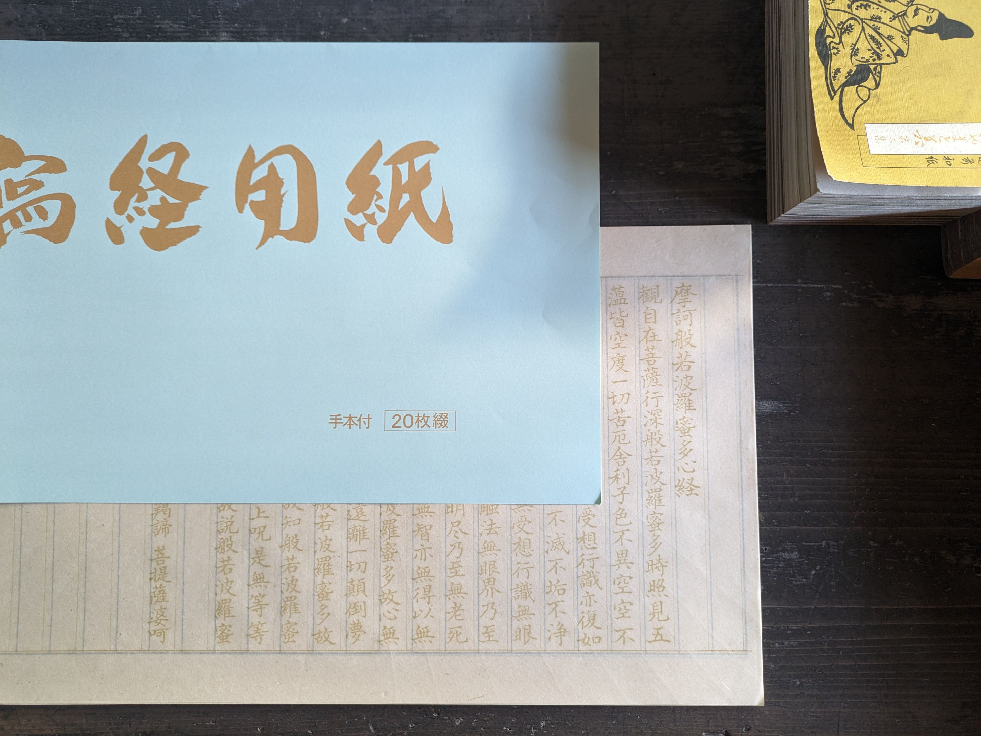 松久永助紙店の蔵出し和紙雑貨、写経用紙の表紙と1枚目を重ねてうつしています。1枚目は金色に近い色でお経が印刷されています。下記は関連するキーワードになります。写経用紙 蔵出し 和紙 美濃和紙 和紙雑貨 写経 禅 ストレス解消 書道 精神安定 ひとりでゆっくり 時間を忘れる 集中 集中力向上 お買い得 販売 ネットショップ 松久永助紙店 近くで和紙が売ってるところ オンラインショップ