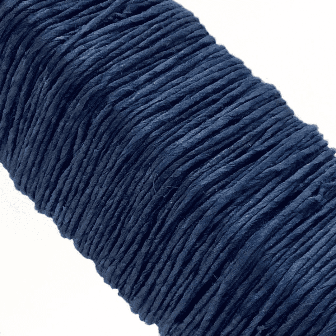 白い背景に、Kamito糸柱の青（藍）がうつっています。糸や色の風合いがわかるようアップで撮影された写真です。原料内訳は美濃和紙100％です。下記は関連するキーワードになります。紙糸 和紙糸 草木染め オリジナル 機械漉き 美濃和紙 自然素材 天然繊維 エコ サスティナブル 環境に優しい 人に優しい ハンドメイド クラフト 材料 素材 ラッピング アクセサリー作り 小物づくり タッセル ニット 編み物 刺繍 青色 紺色 藍色 藍染め 販売 人気 作品 アート 松久永助紙店 オンラインショップ