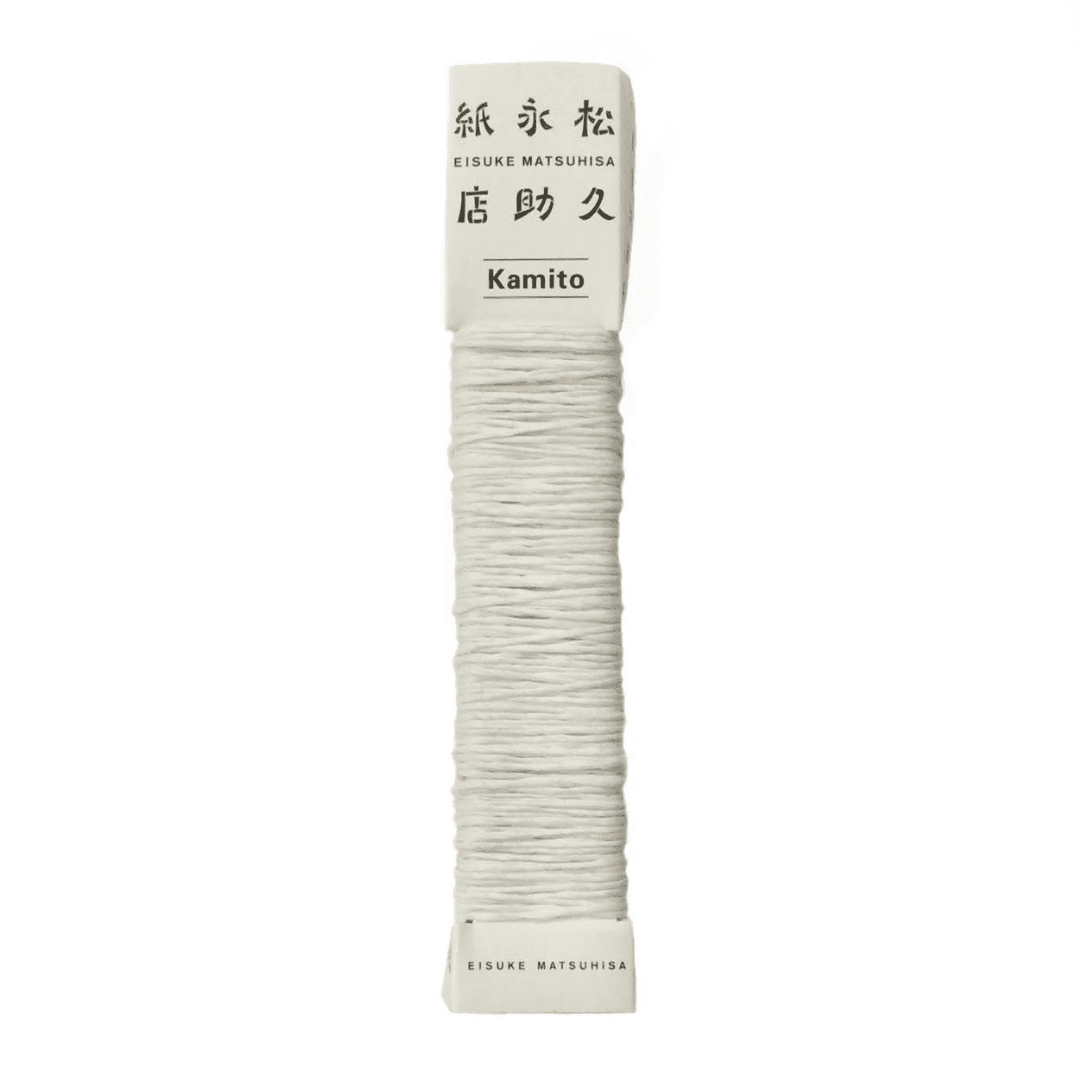 白い背景に、Kamito糸柱の白（染なし）が置かれています。全体像が分かるよう撮影された写真です。糸は店名、商品名が記載された、紙の柱のようなパッケージにまかれています。原料内訳は美濃和紙100％です。下記は関連するキーワードになります。紙糸 和紙糸 草木染め オリジナル 機械漉き 美濃和紙 自然素材 天然繊維 エコ サスティナブル SDGs 環境に優しい 人に優しい ハンドメイド クラフト 材料 素材 ラッピング アクセサリー作り 小物づくり タッセル ニット 編み物 刺繍 ナチュラル 作品 アート 販売 松久永助紙店 オンラインショップ