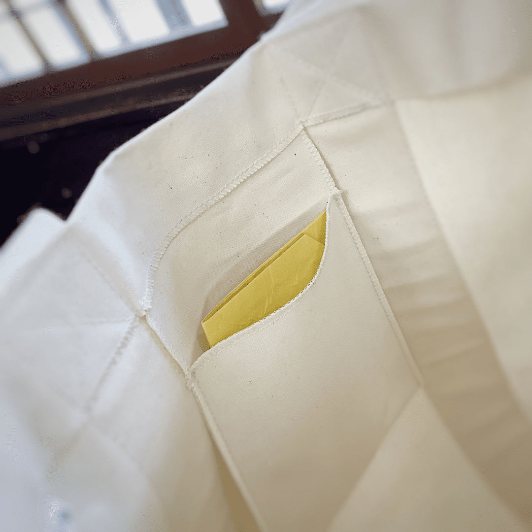 和紙布でできたトートバッグの内ポケットをアップで撮影した写真です。色は生成りです。ポケットの中には、例として黄色いカードケースを入れています。下記は関連するキーワードになります。トートバッグ 軽量 ポケットあり 11号帆布 エコバッグ 普段使い シンプル ギフト おすすめ マチあり こだわり 日本製 松久永助紙店 オンラインショップ