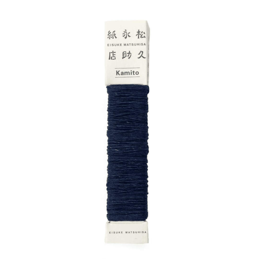 白い背景に、Kamito糸柱の青（藍）が置かれています。全体像が分かるよう撮影された写真です。糸は店名、商品名が記載された、紙の柱のようなパッケージにまかれています。原料内訳は美濃和紙100％です。下記は関連するキーワードになります。紙糸 和紙糸 草木染め オリジナル 機械漉き 美濃和紙 自然素材 天然繊維 エコ サスティナブル 環境に優しい 人に優しい ハンドメイド クラフト 材料 素材 ラッピング アクセサリー作り 小物づくり タッセル ニット 編み物 刺繍 青色 紺色 藍染め アート 作品 人気 販売 松久永助紙店 オンラインショップ