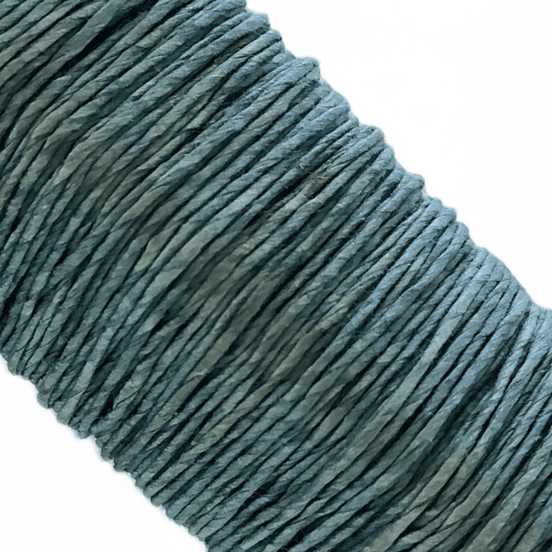 白い背景に、Kamito糸柱の緑（キハダ+藍）がうつっています。糸や色の風合いがわかるようアップで撮影された写真です。原料内訳は美濃和紙100％です。下記は関連するキーワードになります。紙糸 和紙糸 草木染め オリジナル 機械漉き 美濃和紙 自然素材 天然繊維 エコ サスティナブル 環境に優しい 人に優しい ハンドメイド クラフト 材料 素材 ラッピング アクセサリー作り 小物づくり タッセル ニット 編み物 刺繍 緑色 青緑 あるだけ 作品作り 販売 松久永助紙店 オンラインショップ