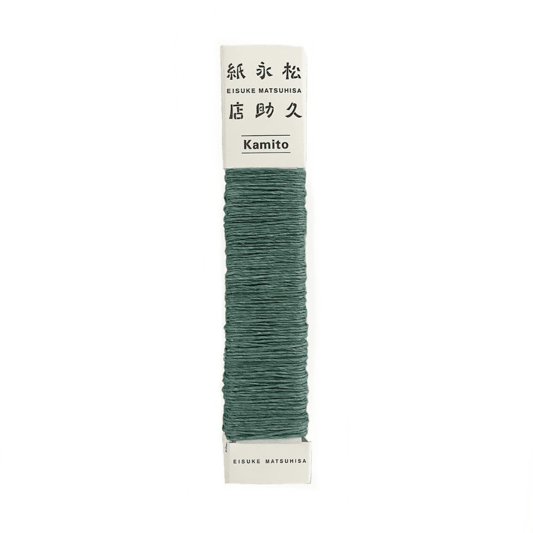 白い背景に、Kamito糸柱の緑（キハダ+藍）が置かれています。全体像が分かるよう撮影された写真です。糸は店名、商品名が記載された、紙の柱のようなパッケージにまかれています。原料内訳は美濃和紙100％です。下記は関連するキーワードになります。紙糸 和紙糸 草木染め オリジナル 機械漉き 美濃和紙 自然素材 天然繊維 エコ サスティナブル 環境に優しい 人に優しい ハンドメイド クラフト 材料 素材 ラッピング アクセサリー作り 小物づくり タッセル ニット 編み物 刺繍 緑色 アート 作品 販売 松久永助紙店 オンラインショップ