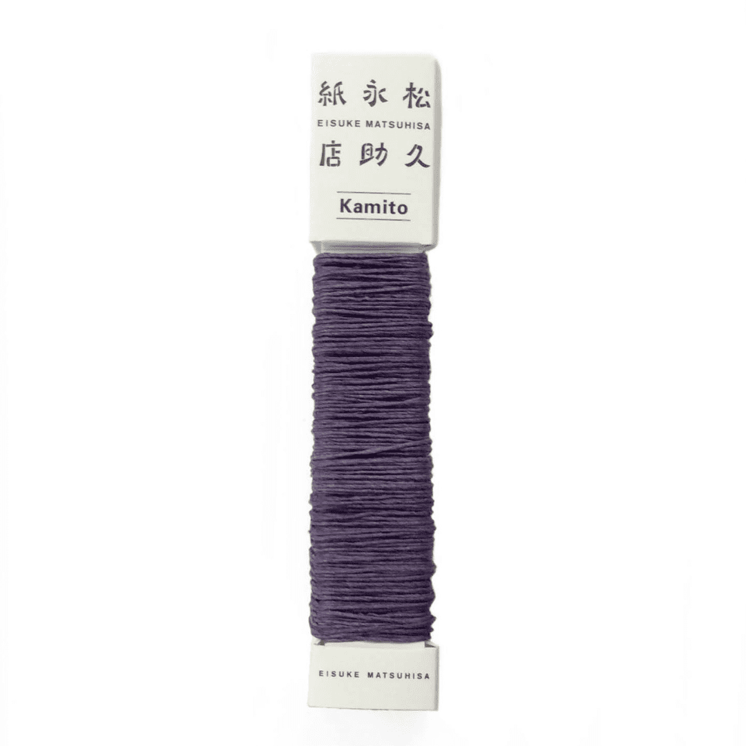 白い背景に、Kamito糸柱の紫（ログウッド）が置かれています。全体像が分かるよう撮影された写真です。糸は店名、商品名が記載された、紙の柱のようなパッケージにまかれています。原料内訳は美濃和紙100％です。下記は関連するキーワードになります。紙糸 和紙糸 草木染め オリジナル 機械漉き 美濃和紙 自然素材 天然繊維 エコ サスティナブル 環境に優しい 人に優しい ハンドメイド クラフト 材料 素材 ラッピング アクセサリー作り 小物づくり タッセル ニット 編み物 刺繍 紫色 自然の色 あるだけ 販売 松久永助紙店 オンラインショップ